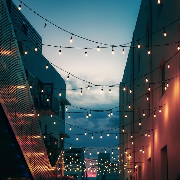 Photo low angle view of illuminated light bulbs amidst building against sky at night