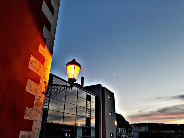 Low angle view of illuminated street light against buildings at sunset