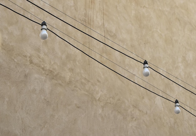 Photo low angle view of light bulbs hanging by concrete wall