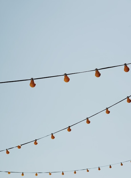 Photo low angle view of light bulbs hanging on cable against clear sky