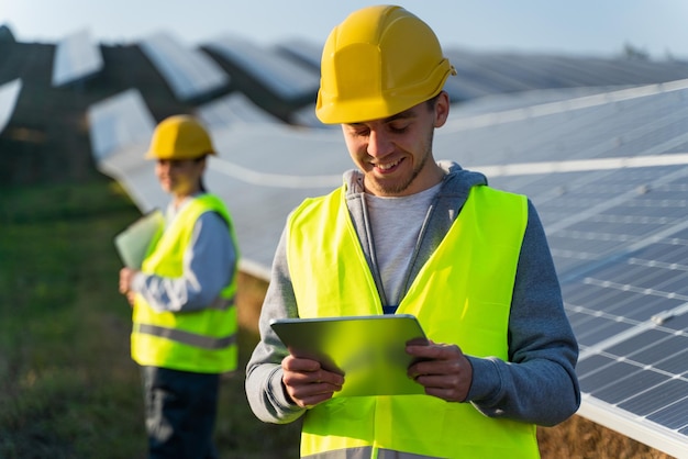 Low angle view of male engineer using tablet solar farm worker\
standing near rows with batteries solar panel field clean energy\
production green energy concept