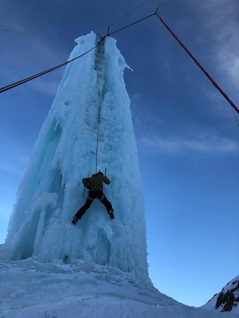 Photo low angle view of man climbing on ice formation against sky during winter