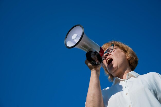 Low angle view of man holding camera against clear blue sky