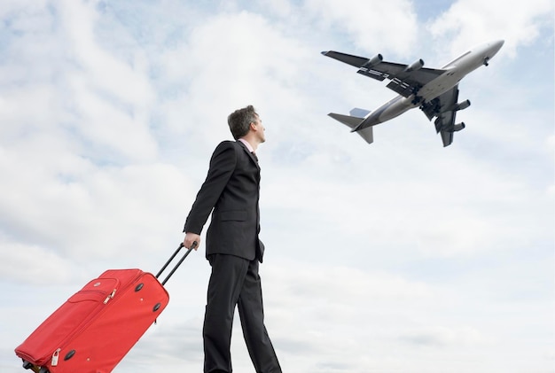 low angle view of man holding luggage while looking at airplane against sky