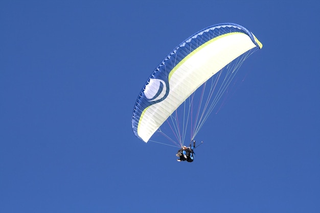 Low angle view of man paragliding in clear blue sky