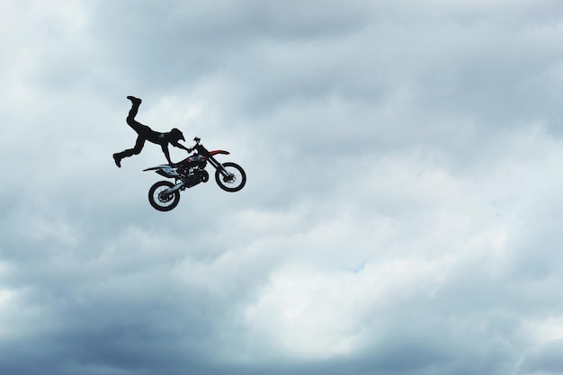 Foto vista a basso angolo di un uomo che esegue una acrobazia su una moto contro un cielo nuvoloso