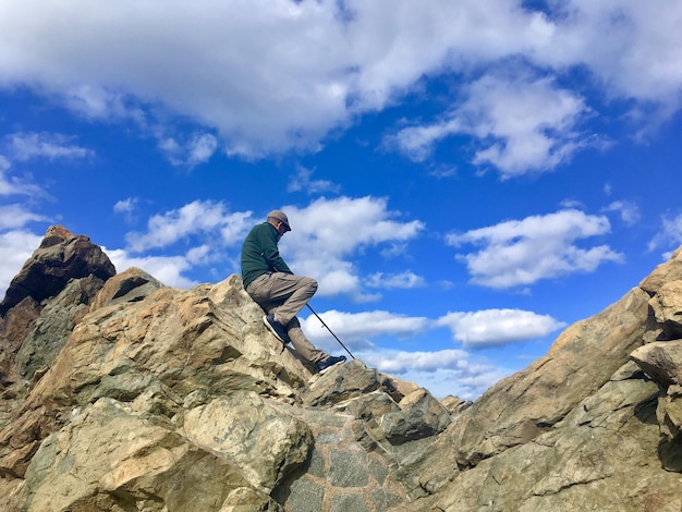 Photo low angle view of man sitting on rocky mountains against sky