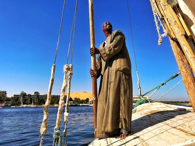 Low angle view of man standing on boat against clear blue sky