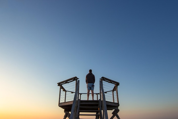 Vista ad angolo basso di un uomo in piedi su un punto di osservazione contro un cielo limpido durante il tramonto