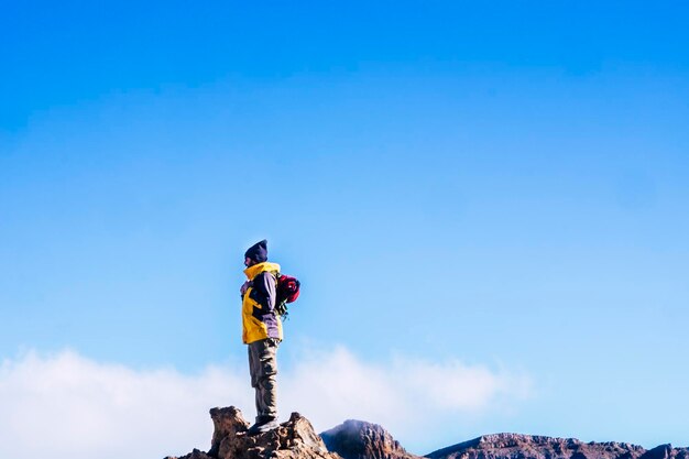 Low angle view of man standing on rock against blue sky