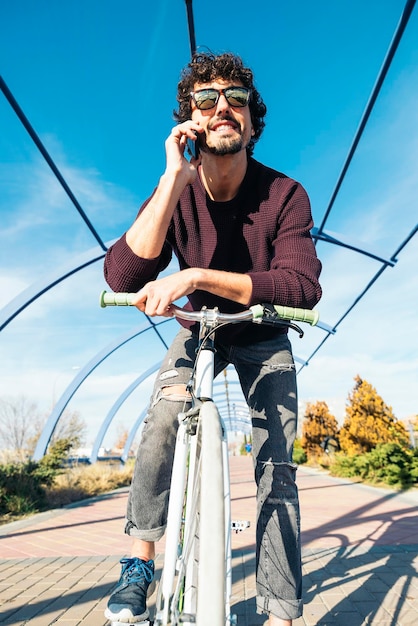 Низкоугольный вид человека, разговаривающего по смартфону, едущего на велосипеде по тропинке напротив неба