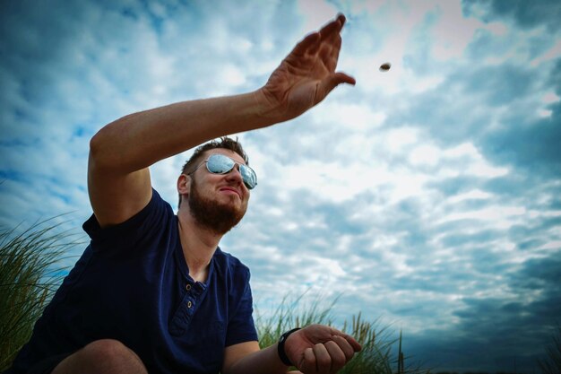 Foto vista a bassa angolazione di un uomo che lancia una pietra contro un cielo nuvoloso