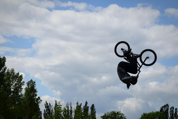 Low angle view of man with bicycle in mid- air against cloudy sky