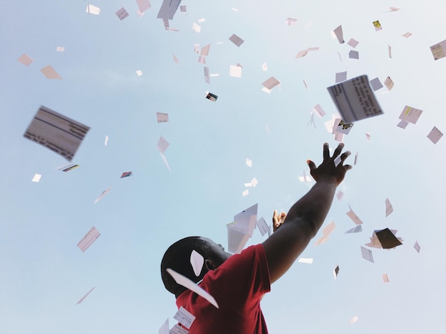 Photo low angle view of man with papers falling against sky