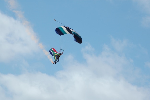 Photo low angle view of man with south african flag paragliding against cloudy sky