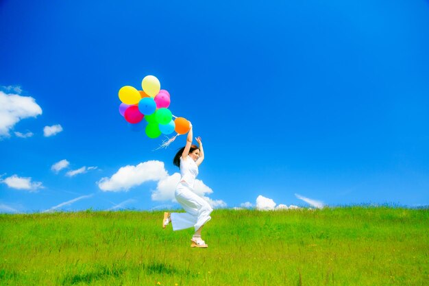 Low angle view of mature woman jumping with balloons on grassy field