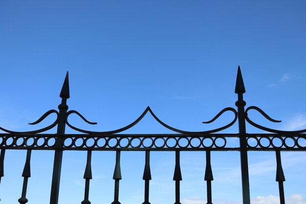 Low angle view of metal fence against blue sky