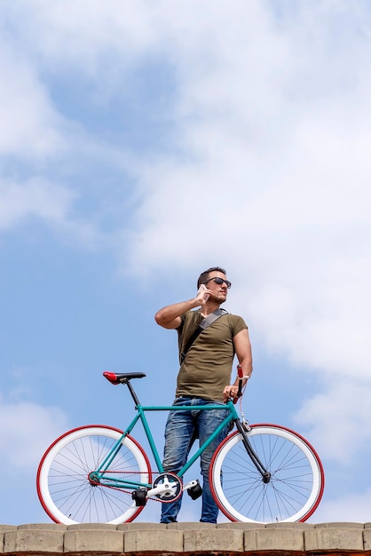 Низкий угол зрения среднего взрослого человека, разговаривающего по мобильному телефону, стоя с велосипедом на небе