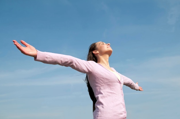 Low angle view of mid adult woman with arms outstretched standing against blue sky