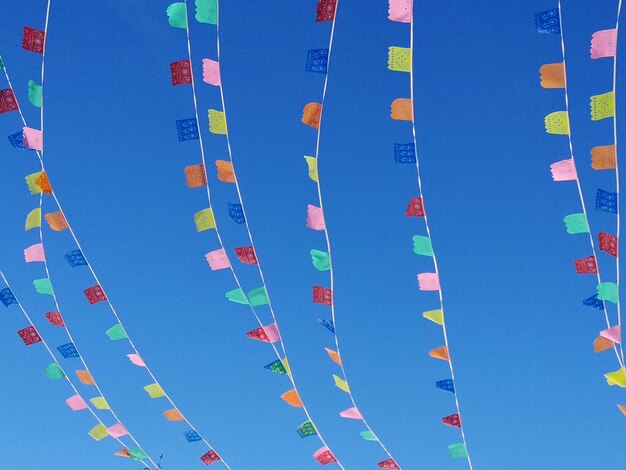 Low angle view of multi colored flags against blue sky