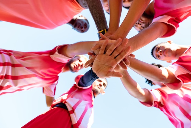 Foto vista a basso angolo dei giocatori di una squadra di calcio maschile multirazziale che si impilano le mani prima della partita sul parco giochi