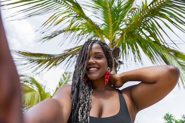 사진 셀카를 찍는 쾌활한 아프리카계 미국인 여성의 낮은 각도 보기. 웃 고 카메라를 보고 해변에서 아름 다운 성인 여자.