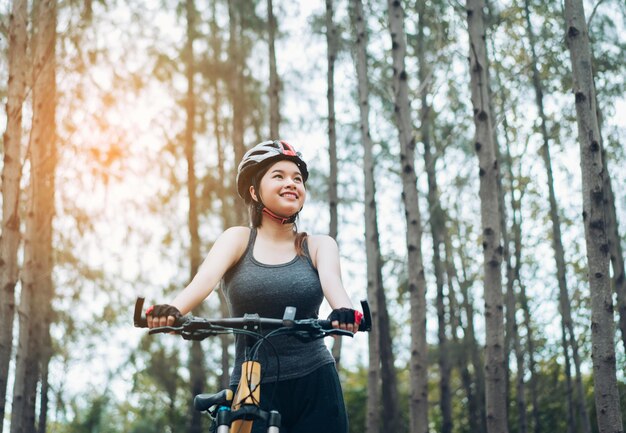 写真 森で自転車に乗って立っている幸せな女性サイクリストの低角度の写真