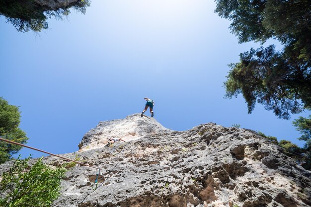 写真 明るい青い空の背景に山を登っている男性友達の低角度の写真