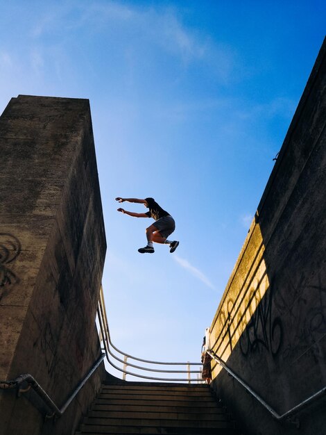 Фото Низкий угол зрения человека, прыгающего над ступеньками на синем небе
