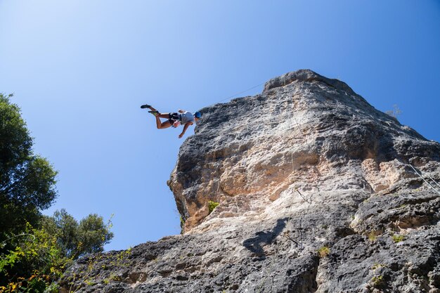 写真 明るい青い空を背景に岩を登る男の低角度の景色