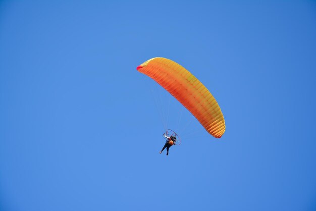 Фото Низкоугольный вид человека, катающегося на параплане на чистом голубом небе