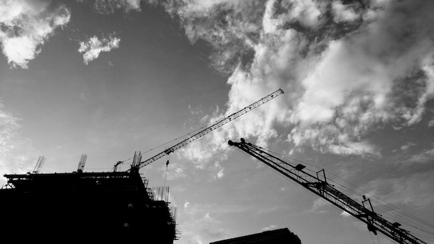 Фото Низкий угол изображения силуэтных кранов на строительной площадке на фоне неба
