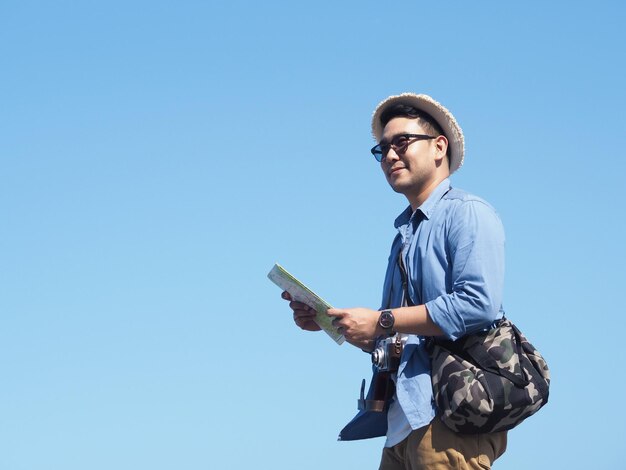 写真 明るい青い空を背景に地図を持って立っている笑顔の男の低角度の視点