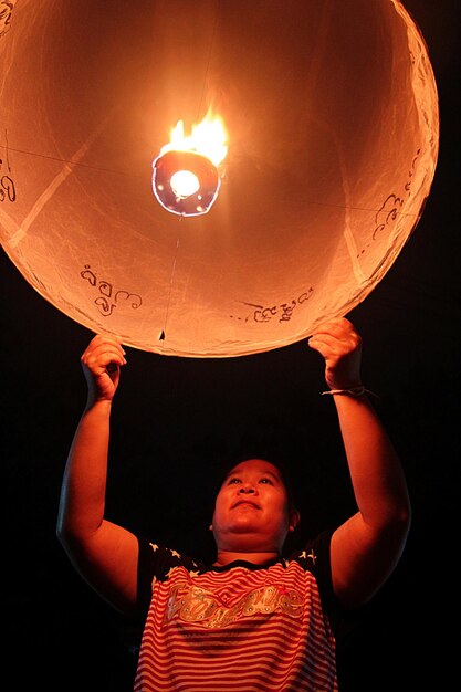 Фото Низкий угол зрения женщины, держащей освещенный бумажный фонарь против неба ночью