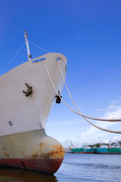 Low angle view of oil tanker moored at harbor against blue sky background in vertical frame