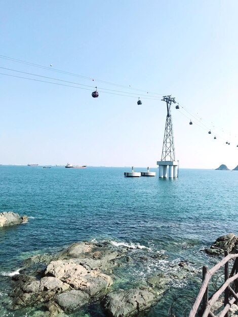 Low angle view of overhead cable car over sea against clear sky