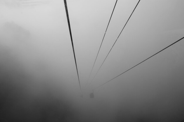 Low angle view of overhead cable cars against sky during foggy weather