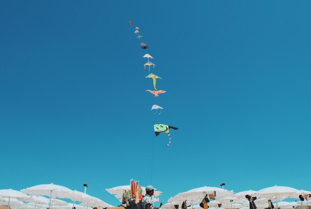 Photo low angle view of people flying kites against clear blue sky