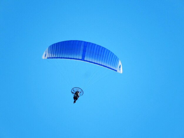 Foto vista a basso angolo di una persona in parapendio contro un cielo blu limpido