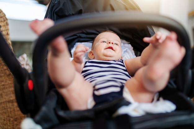 6 개월 장난 백인 행복 한 아기의 낮은 각도보기 유모차에 앉아 찾고 스트라이프 아기 옷을 입고.