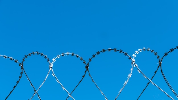 Low angle view of razor wire fence against clear blue sky