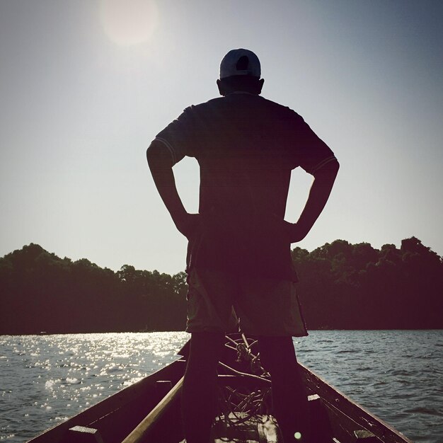 Low angle view rear view of man standing on boat on sunny day