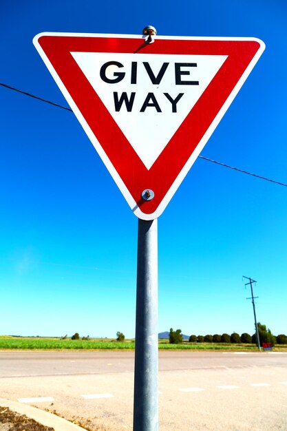 Low angle view of road sign against clear blue sky