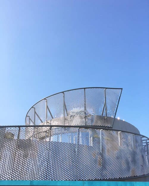 Low angle view of rollercoaster against clear blue sky