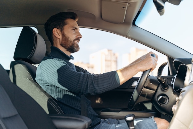low angle view of the serious confident man riding at the car and looking at the road during driving. stock photo