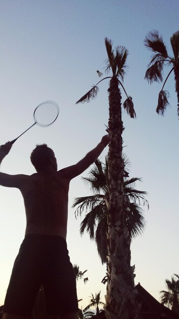 Foto vista a basso angolo di un uomo senza camicia che gioca a badminton contro il cielo durante il tramonto