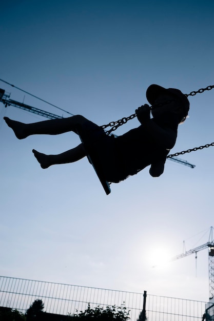 Foto vista a basso angolo di un ragazzo a silhouette che si diverte a oscillare contro un cielo blu limpido