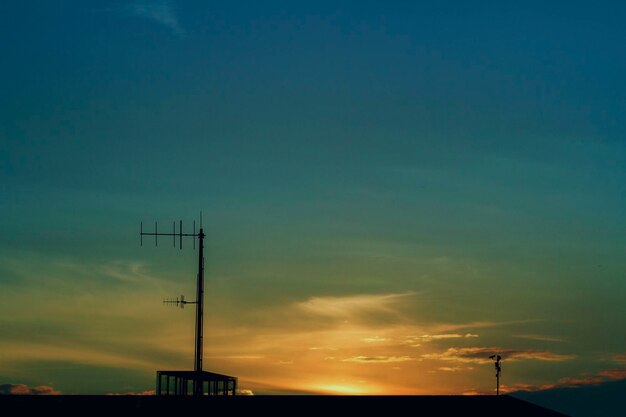 Low angle view of silhouette communications tower against sky during sunset