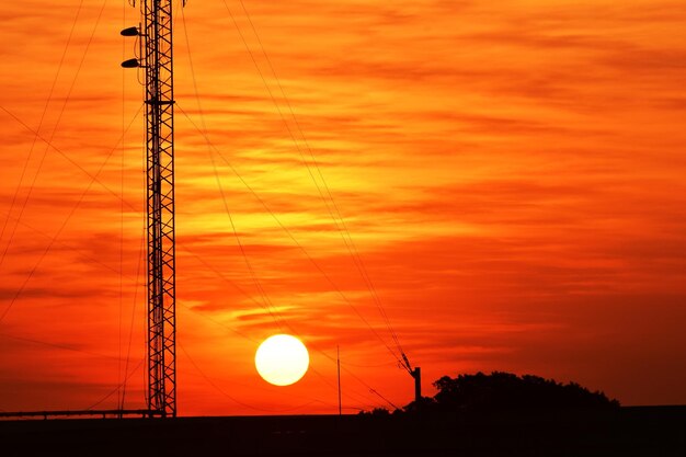 Low angle view of silhouette electricity pylon against orange sky