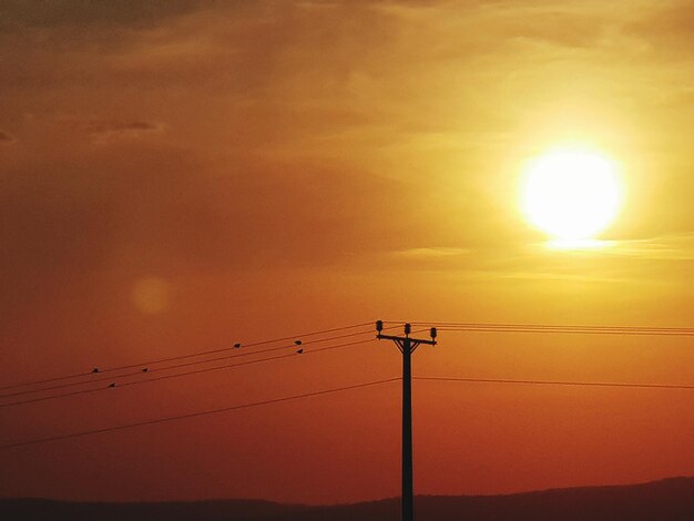 Low angle view of silhouette electricity pylon against sky during sunset